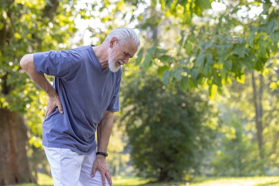 Mature man experiencing sciatic nerve pain in lower back outdoors