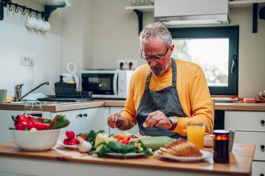 Senior man preparing a healthy Mediterranean-style meal in kitchen — the best dietary pattern for hearing preservation