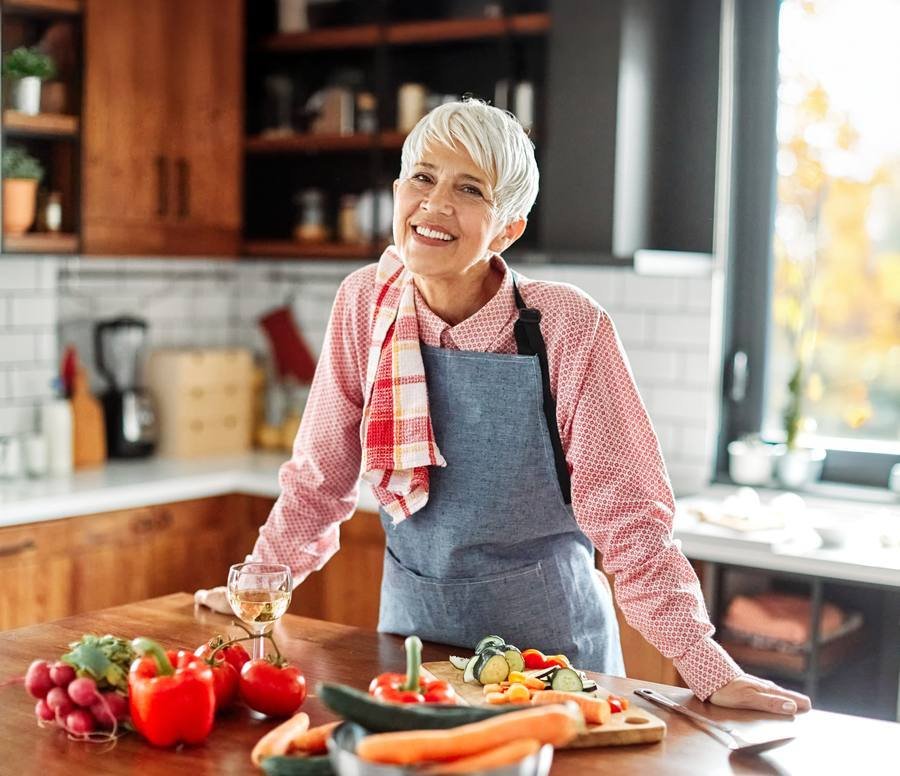 Smiling woman in kitchen preparing healthy meal — sustainable weight management after 40