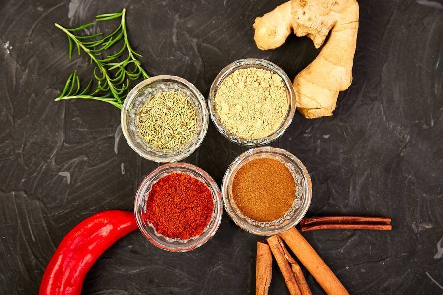 Natural thermogenic spices — cayenne pepper, ginger, cinnamon, and rosemary on dark surface
