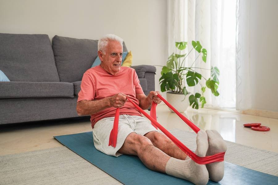 Senior man performing resistance band rowing exercise at home for spinal strength