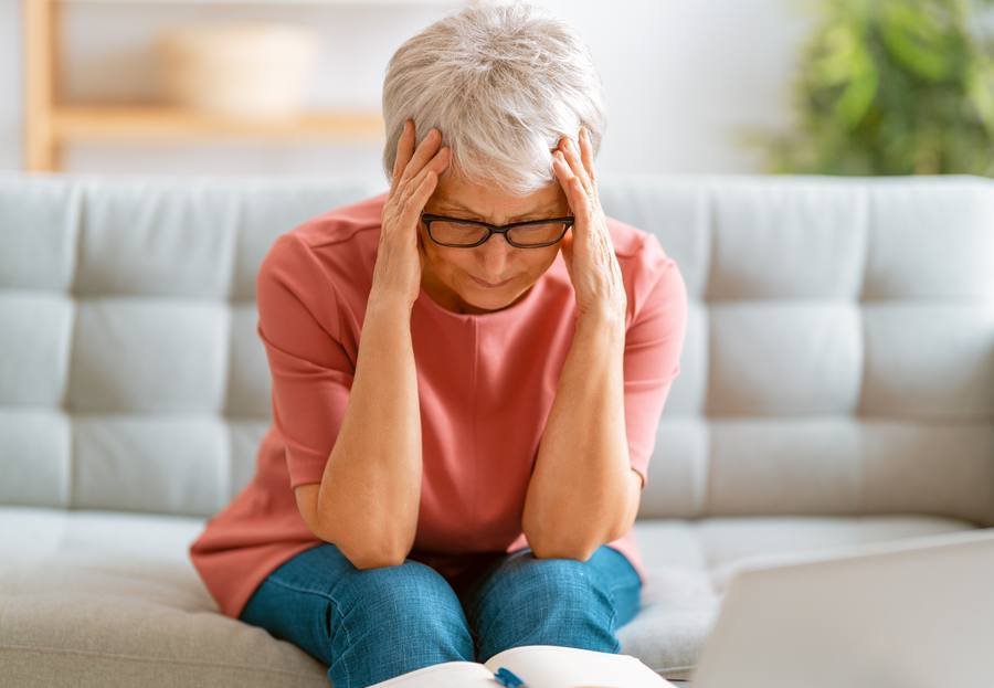 Senior woman holding head in stress — cortisol worsens tinnitus symptoms