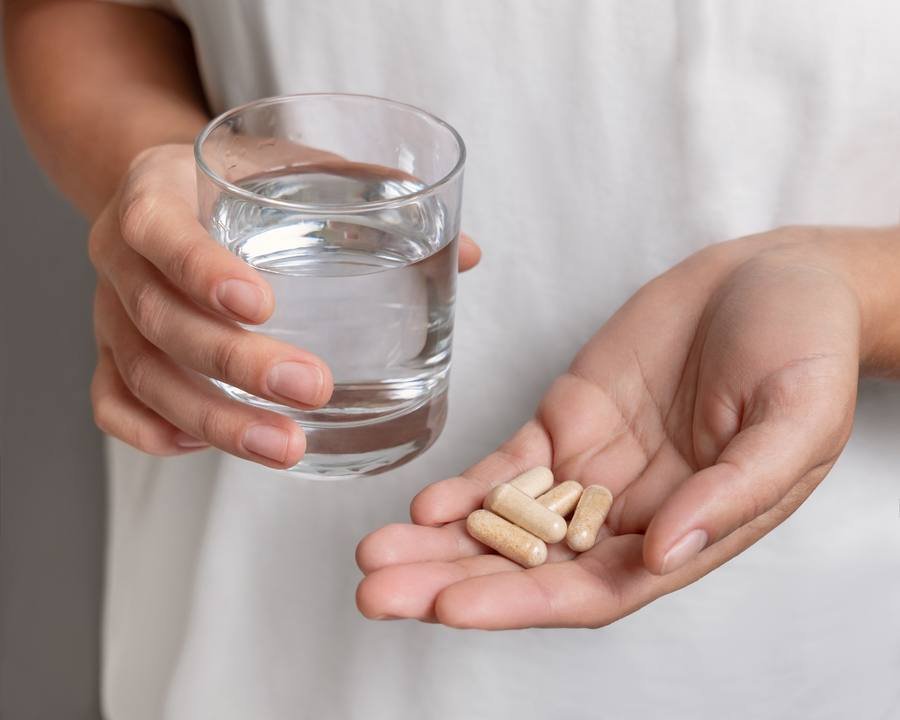 Person holding natural supplement capsules with glass of water for nerve health support