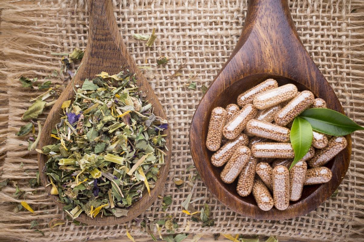 Dried herbs and natural capsules on wooden spoons