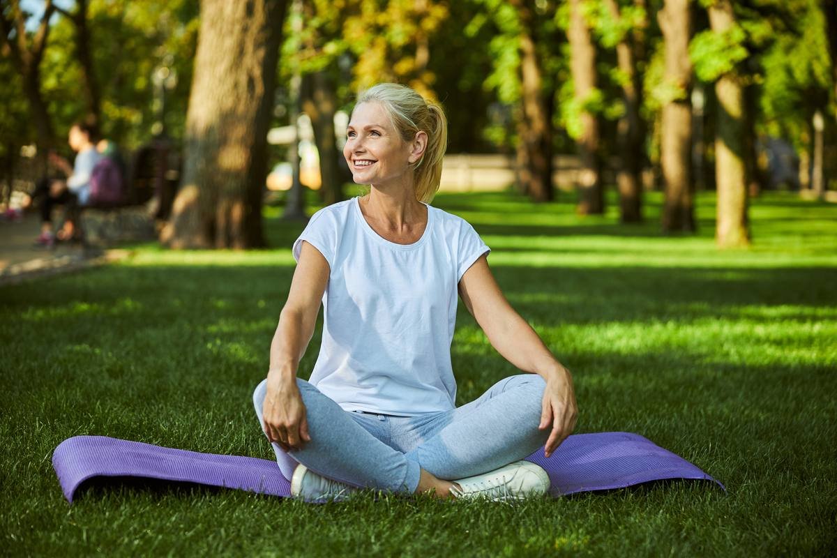 Mature woman relaxing on yoga mat outdoors — women's wellness after 40